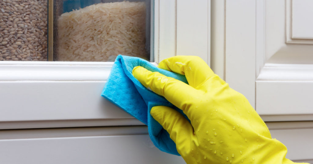 Cleaning and wiping the doors of the facade of the kitchen cabinet. Hand in a yellow glove with a blue rag 