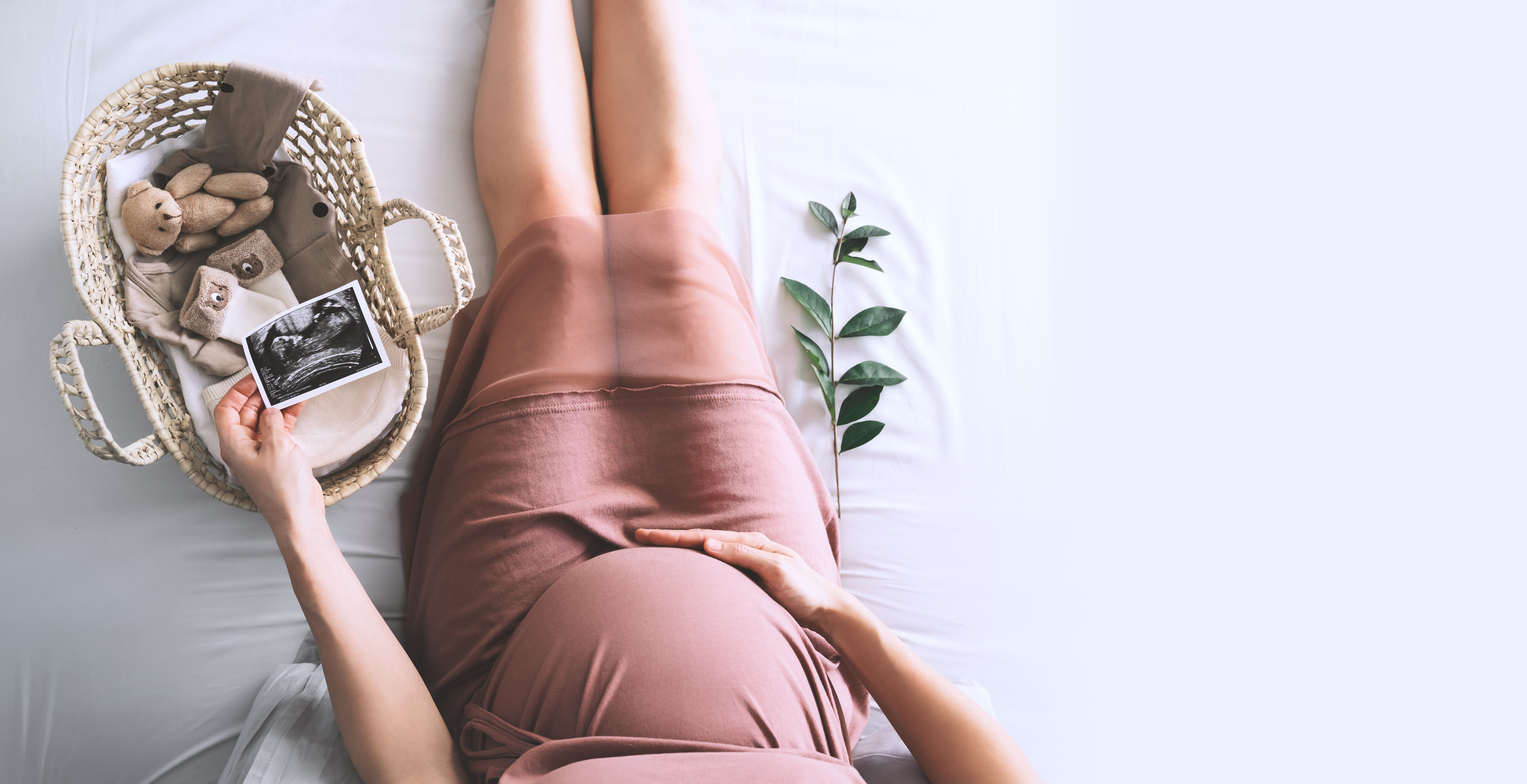 A woman holding a scan of her baby in one hand and her pregnant belly in the other next to a basket of baby supplies | Source: Shutterstock