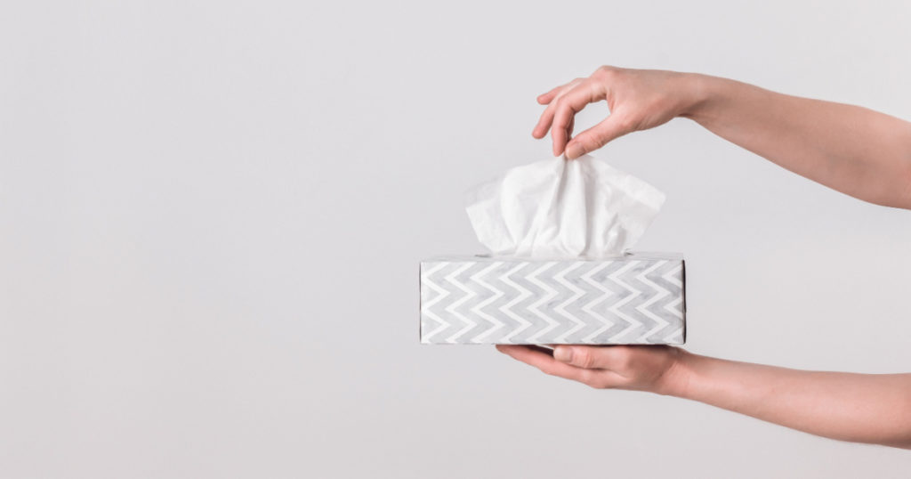 Delicate female hands pulling a tissue out of a gray tissue box. 