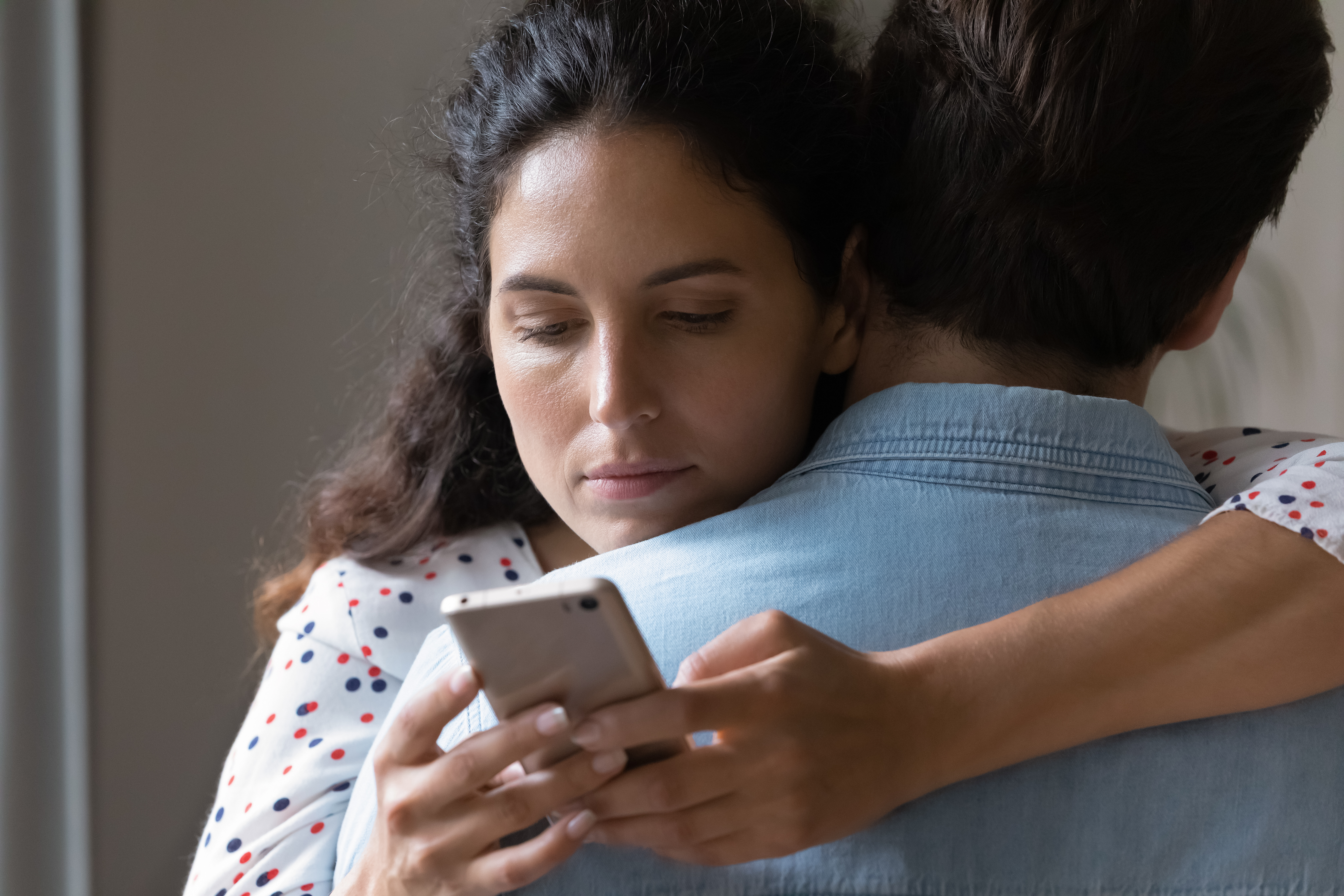 A man and a woman hugging while she looks at her phone | Source: Shutterstock