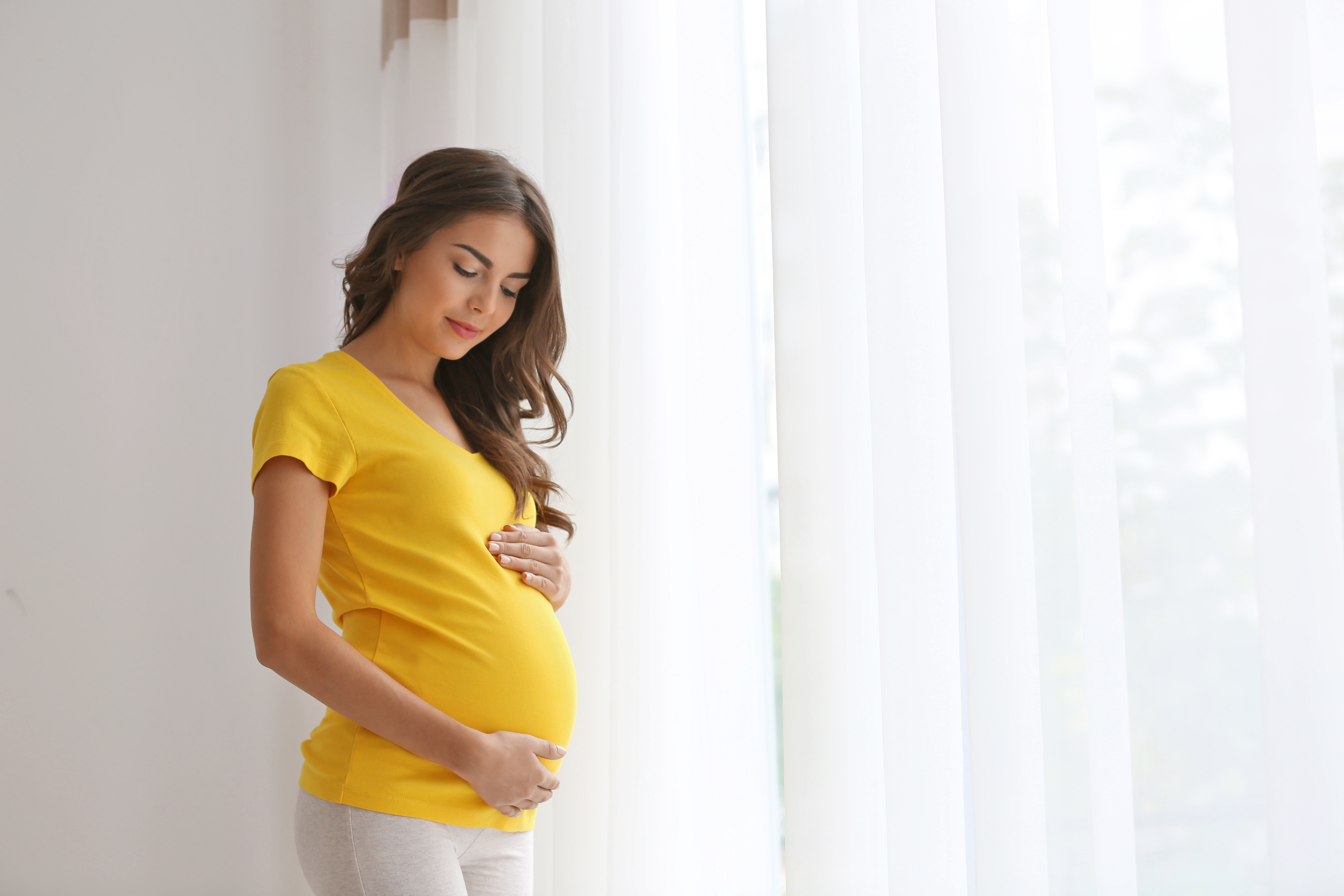 A pregnant woman in a yellow shirt holding her belly | Source: Shutterstock