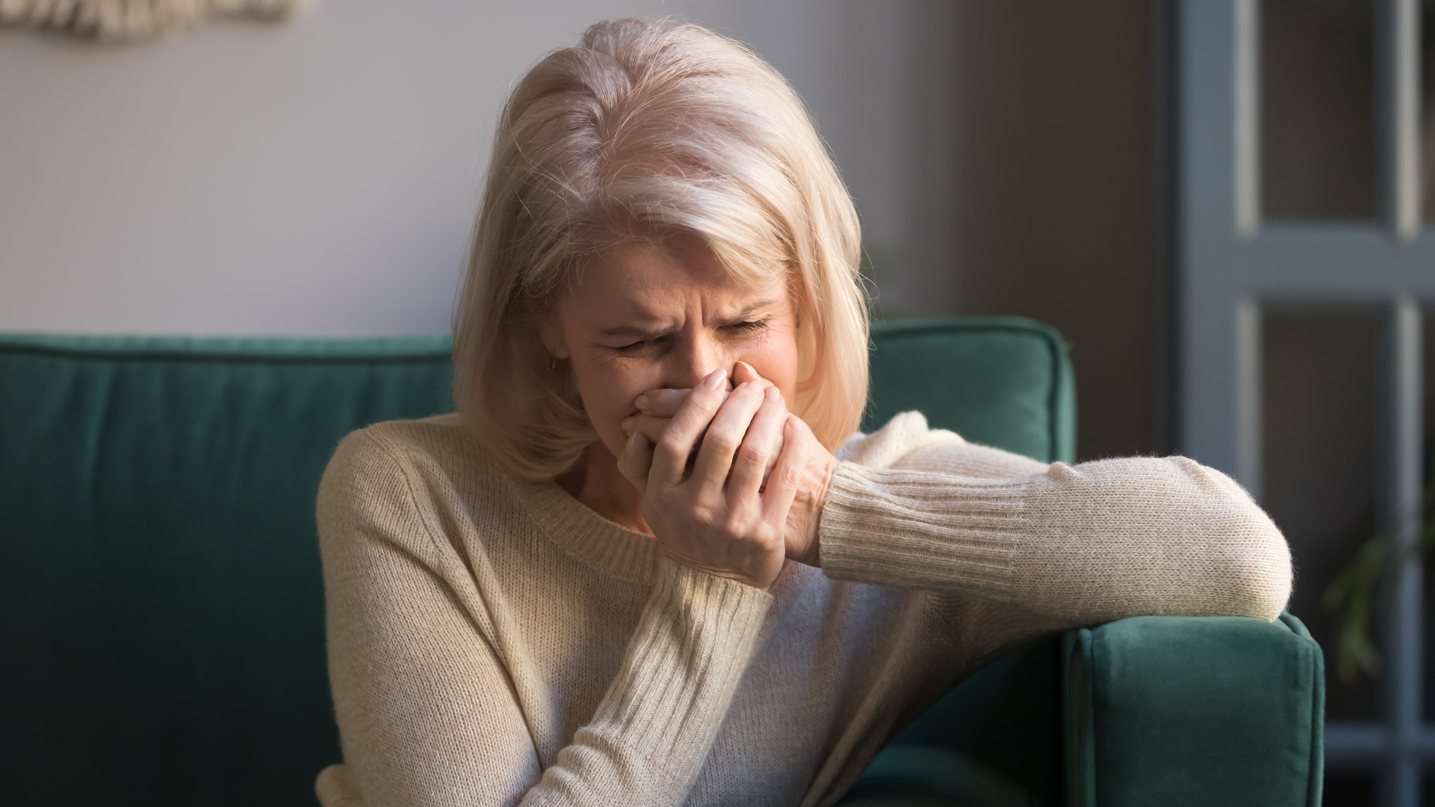 A senior woman crying while sitting on the sofa | Source: Shutterstock
